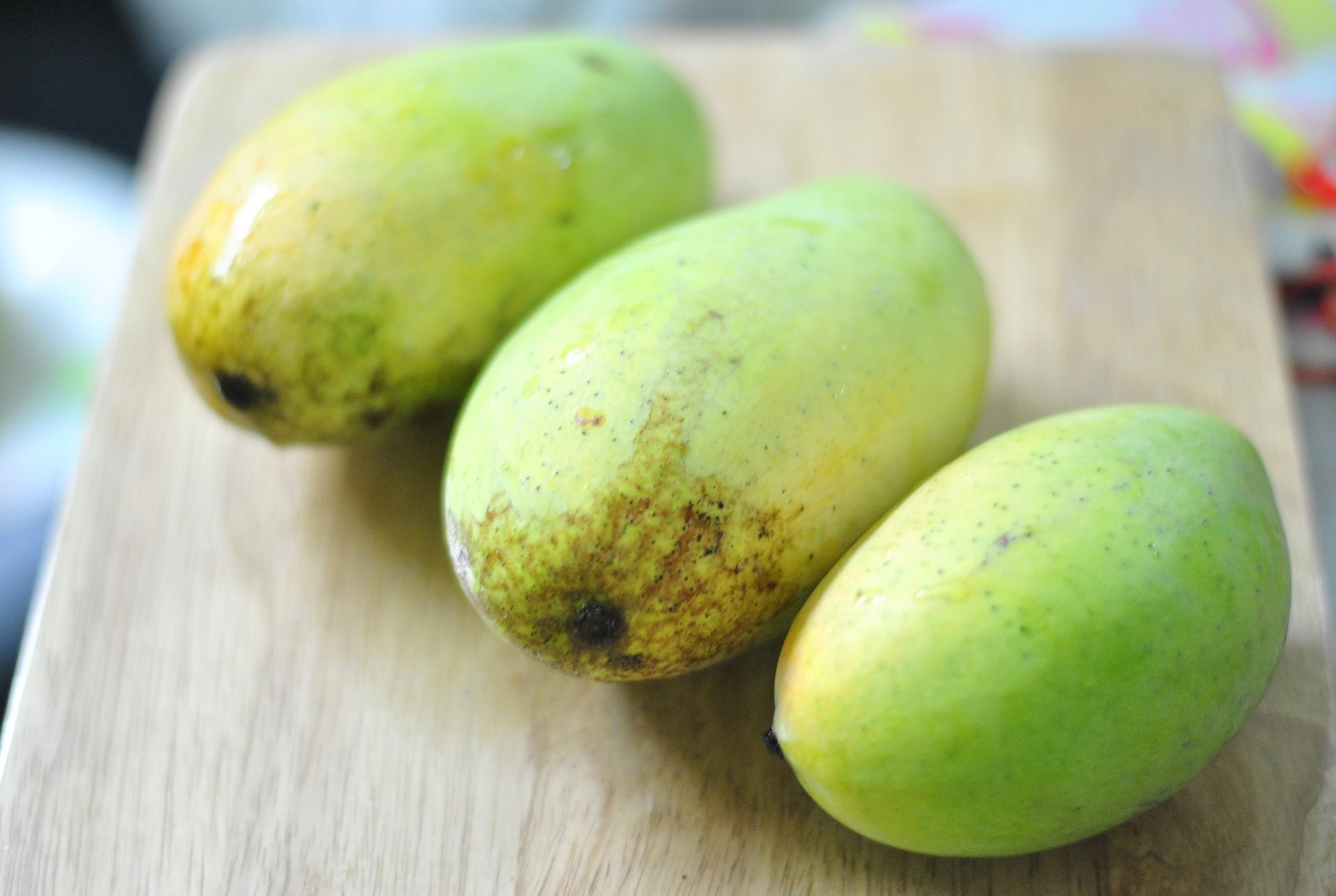 Three green mangoes on a cutting board