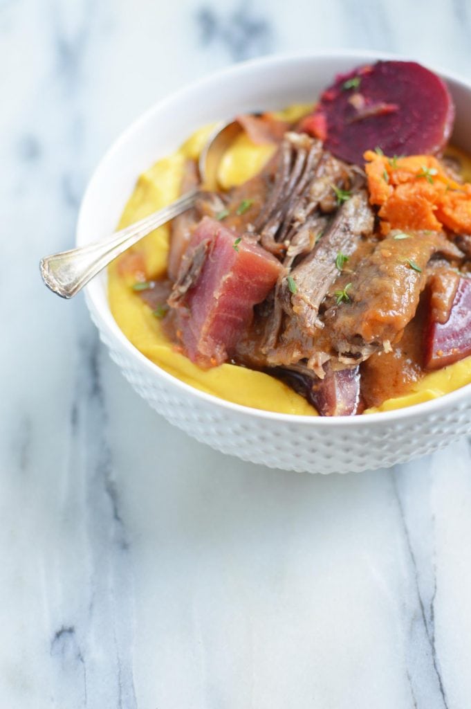 Instant Pot Short Ribs with Vegetables, short ribs with veggies in a white bowl with spoon sitting on a white and grey marble table top.