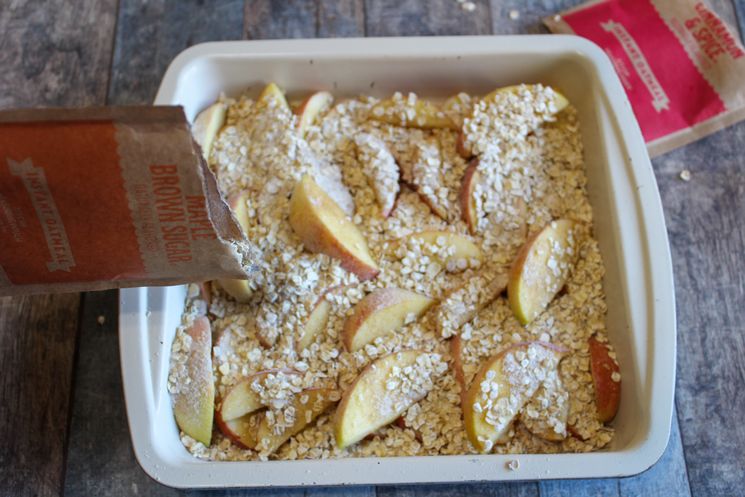 Baking dish with apples being sprinkled with instant oatmeal from the packet