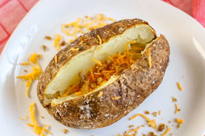 Air fryer baked potato topped with shredded cheddar cheese and bacon bits