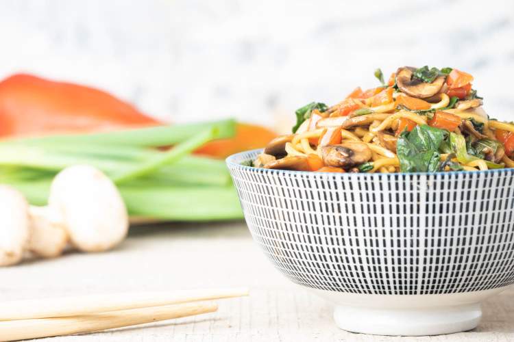 Spinach and mushroom lo mein served in an Asian style bowl with chopsticks next to it.
