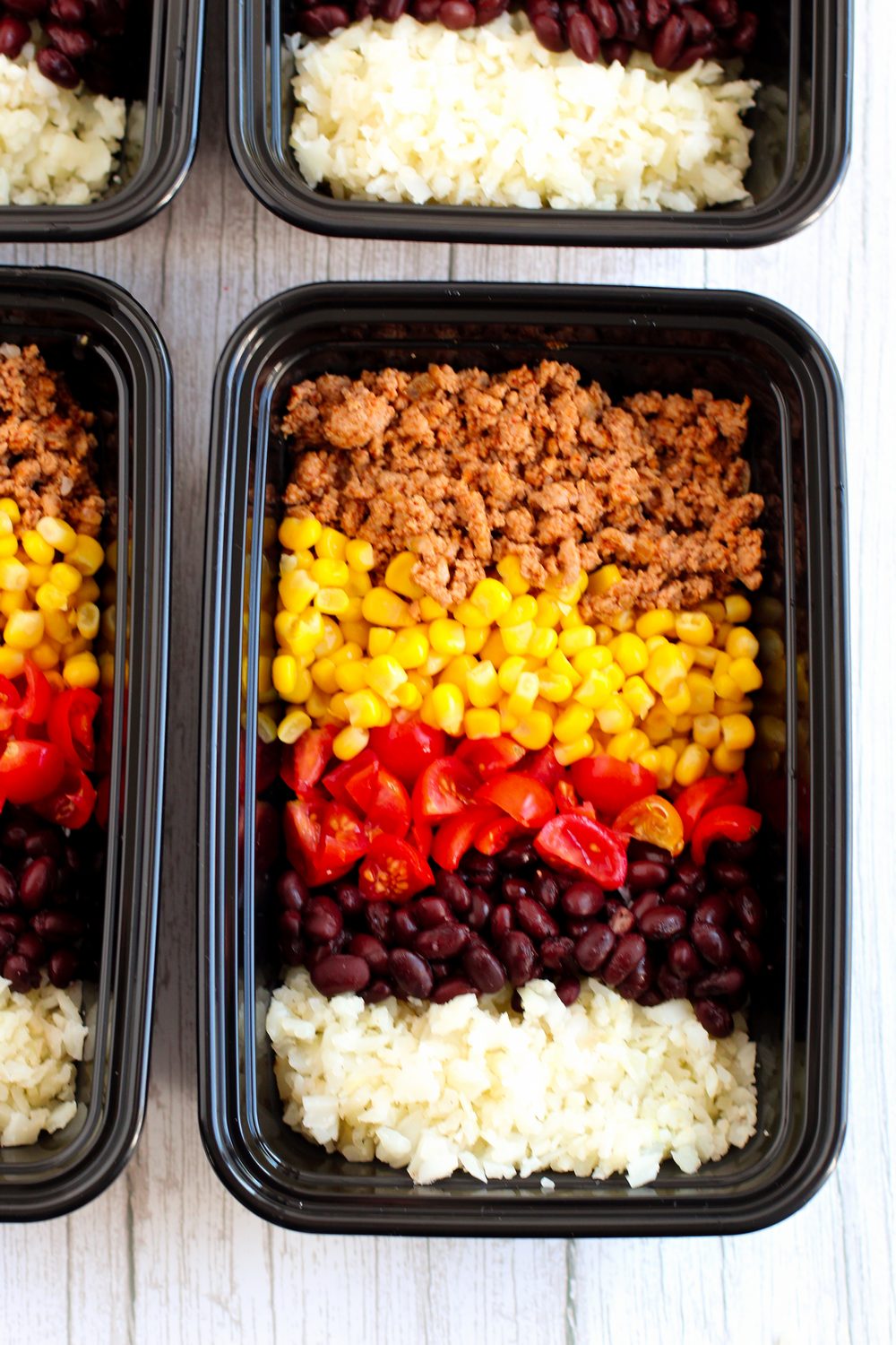 add corn and tomatoes to meal prep containers with meat and cauliflower rice